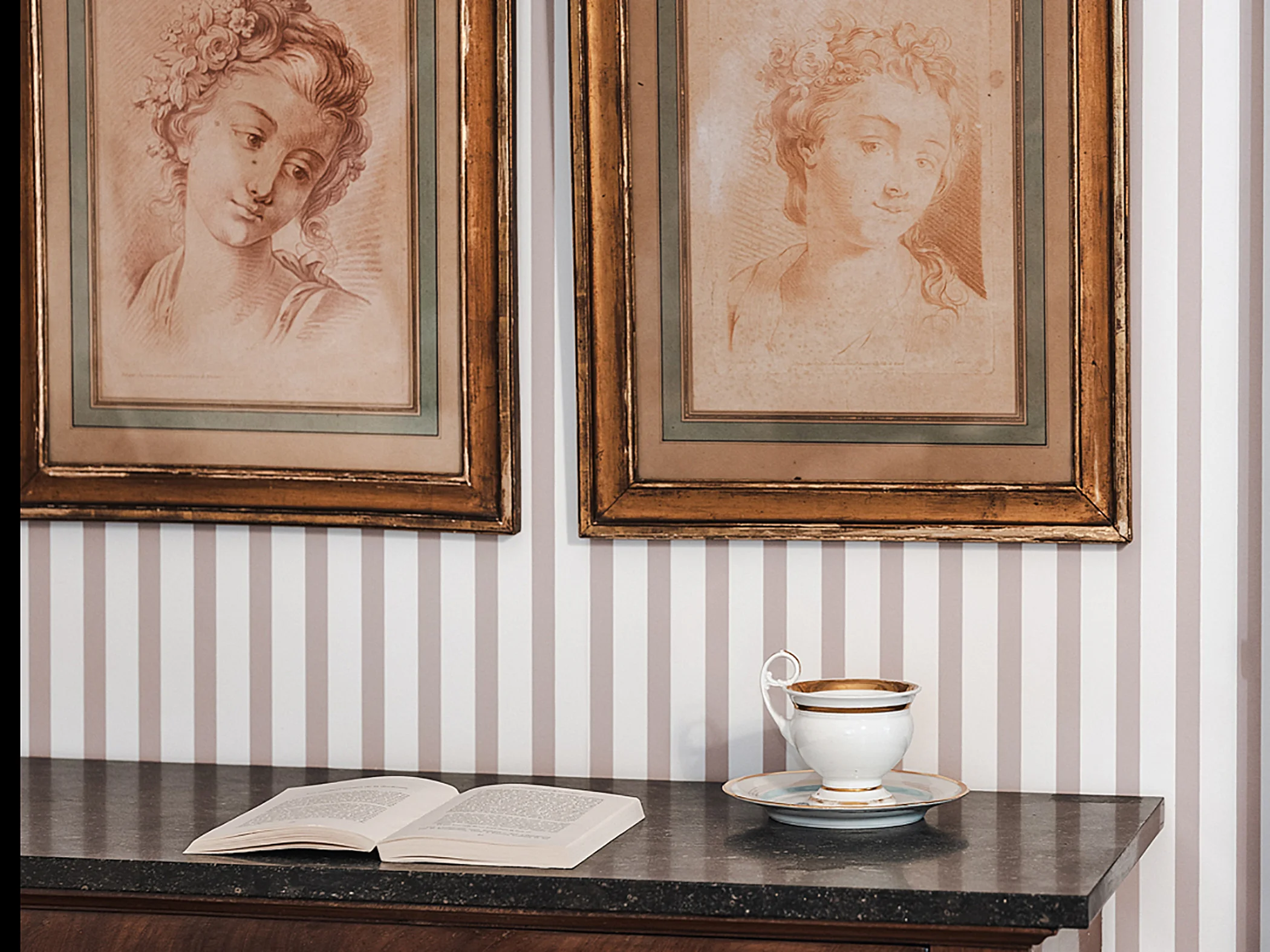 Deux portraits anciens encadrés accrochés au-dessus d'un meuble avec un livre ouvert et une tasse à café.
