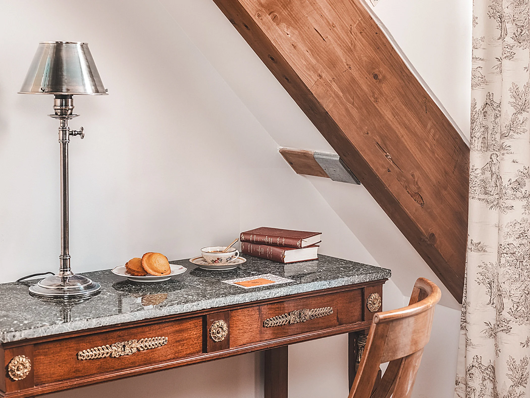 Bureau en bois surmonté d'une lampe de table élégante, avec des livres et une petite assiette de collations.