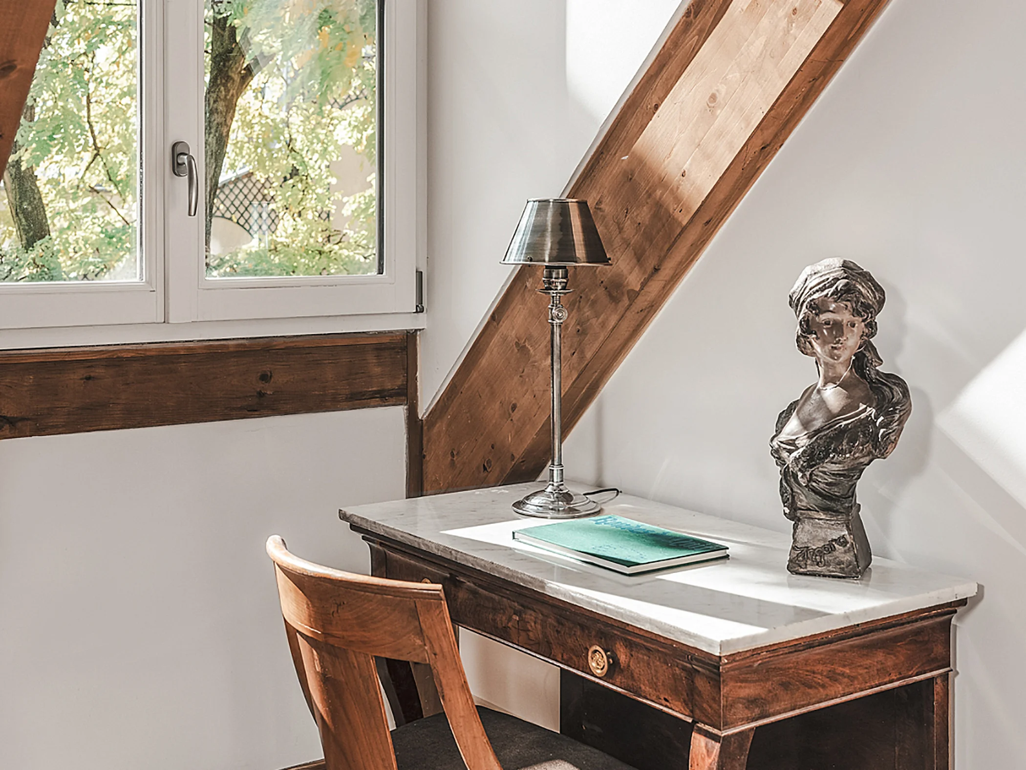 Bureau en bois ancien et lampe classique près d'une fenêtre mansardée.