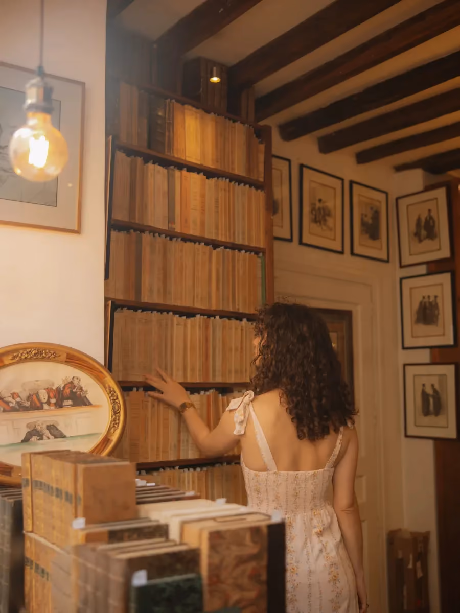 Femme aux cheveux bouclés choisissant un livre dans une bibliothèque ancienne.