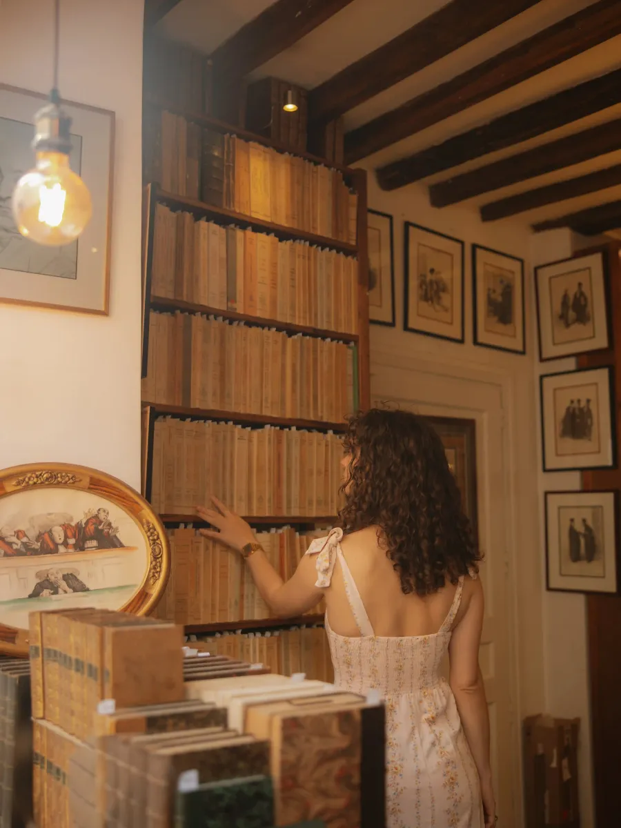 Femme aux cheveux bouclés choisissant un livre dans une bibliothèque ancienne.