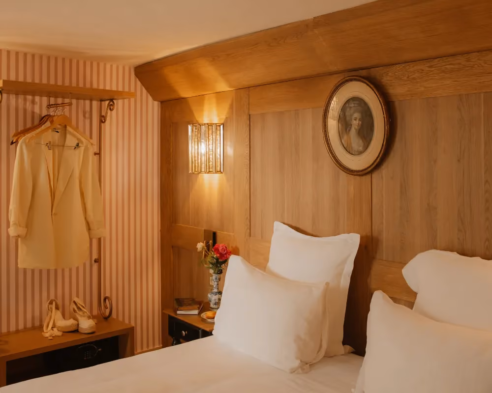 Intérieur de chambre avec un lit douillet, une veste sur un portant et un portrait mural ovale.