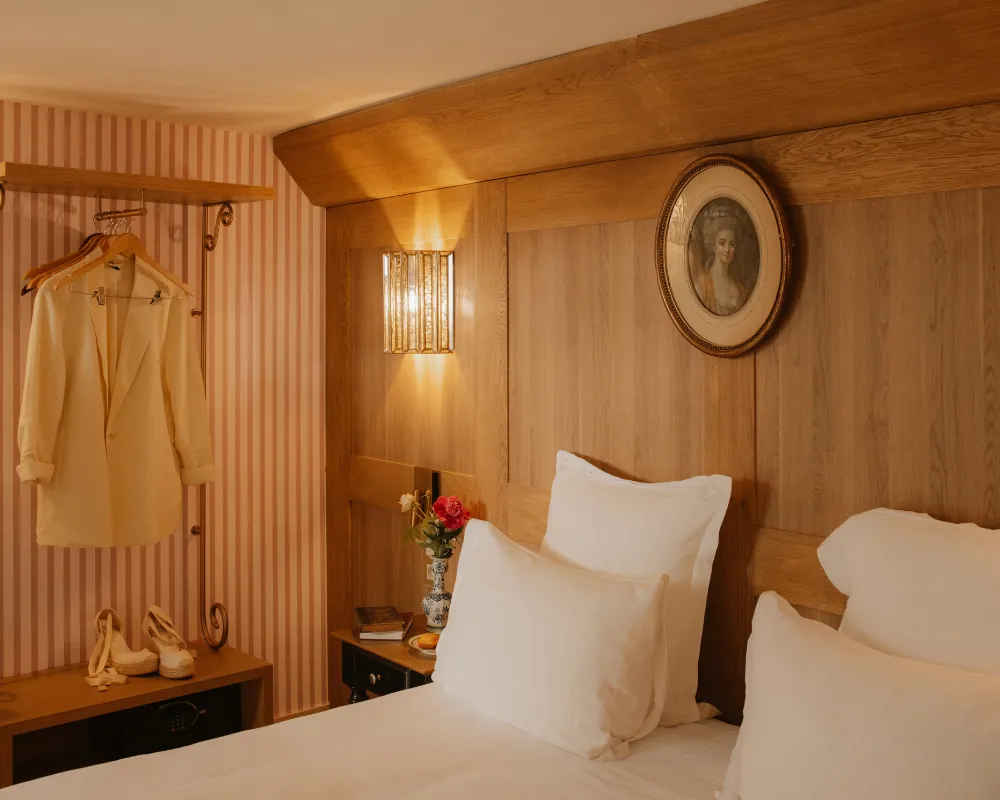 Intérieur de chambre avec un lit douillet, une veste sur un portant et un portrait mural ovale.