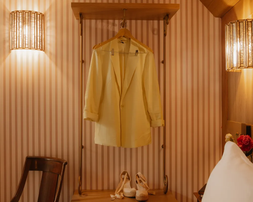 Veste beige élégante suspendue à un portant en métal, accompagnée d'une paire d'espadrilles au sol.