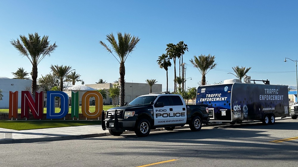 Police truck labeled Indio Police parked near colorful Indio city sign with palm trees in background.