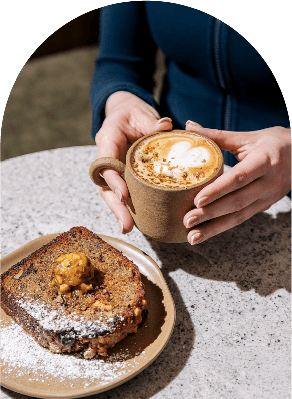 Imagen de persona sosteniendo una taza de chai acompañado de un pan de plátano