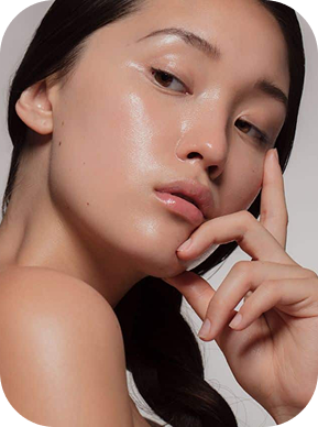 Close-up of a woman with glossy, smooth skin posing with her hand near her face.