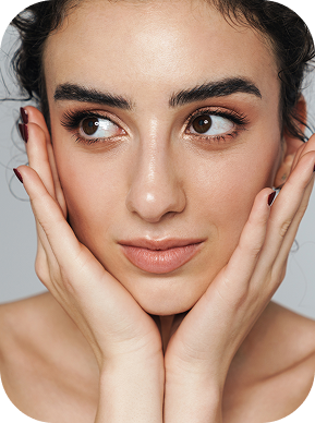 Close-up of a woman with clear skin and dark hair holding her face in her hands, looking to the side.