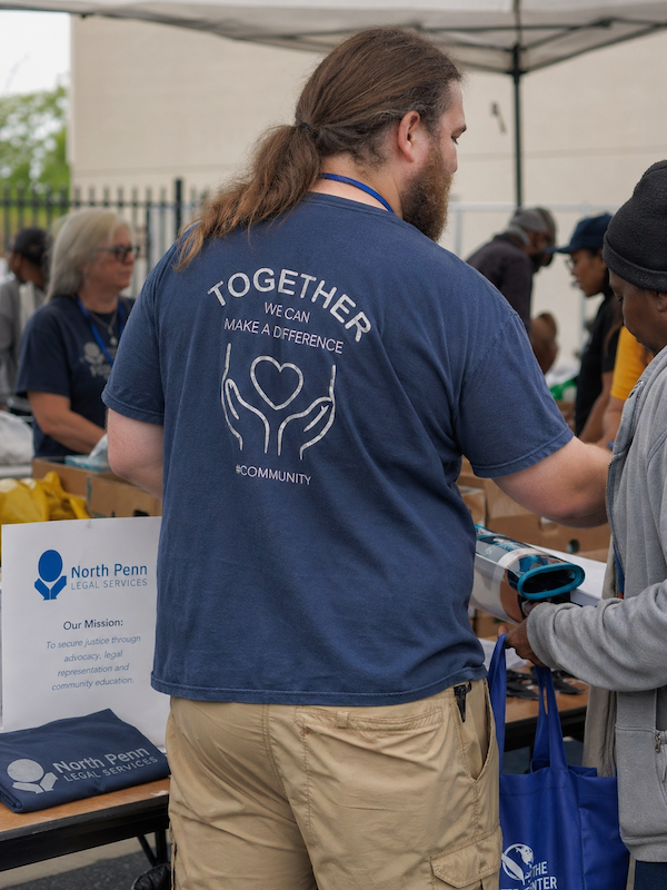 Volunteer wearing a blue shirt with 'Together We Can Make a Difference #Community' helping at a North Penn Legal Services event.