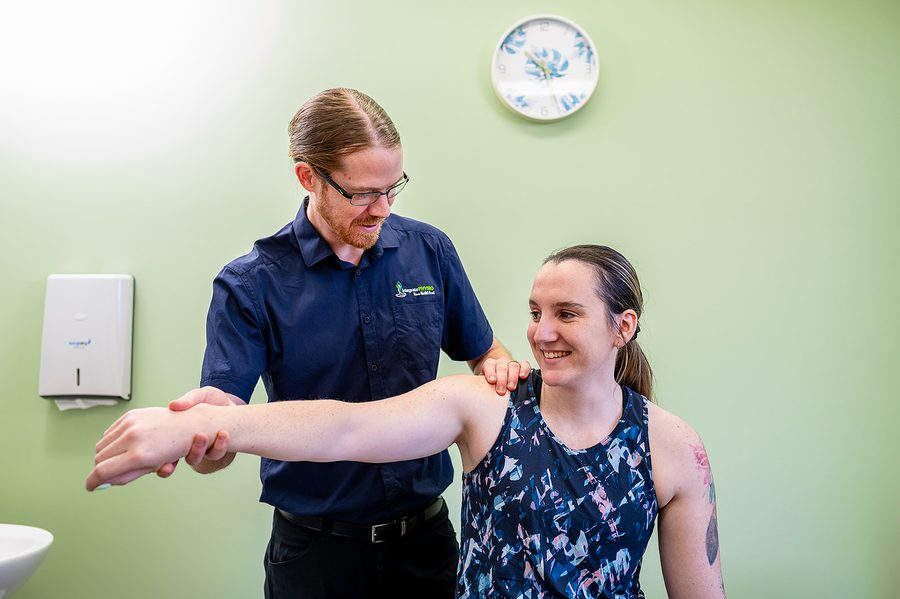 Physiotherapist assisting a smiling woman with shoulder exercise in a clinic room.