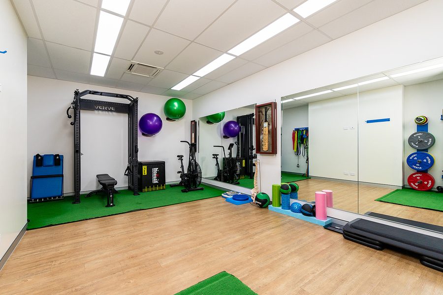 Integrate Physio gym room with exercise bikes, weight rack, fitness balls, and foam rollers on wooden floor.