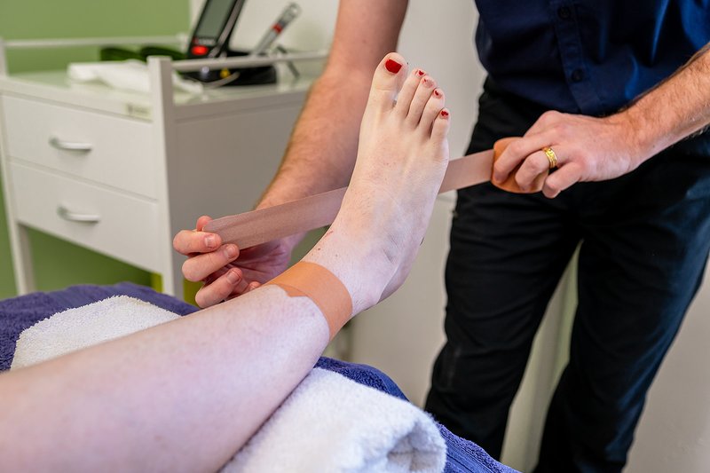 Healthcare professional wrapping a bandage around a person's ankle in a clinical setting.