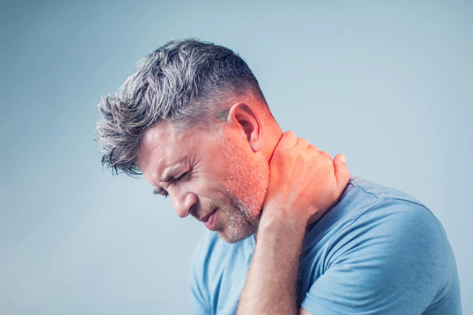 Man in blue shirt holding neck with a pained expression indicating neck pain.