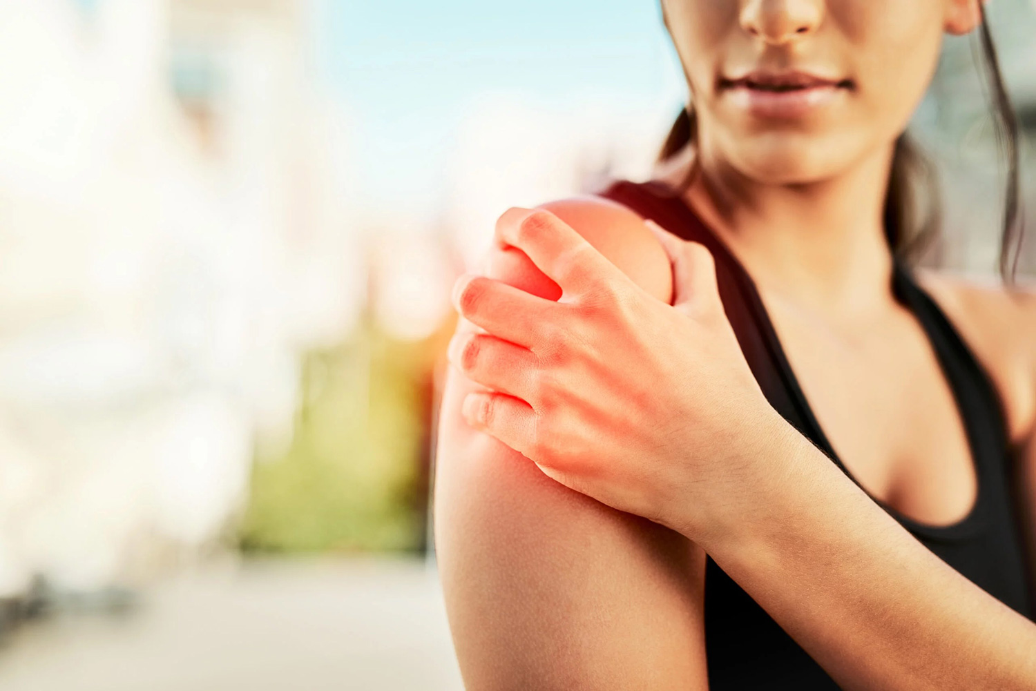Woman in black sportswear holding her shoulder in pain outdoors.