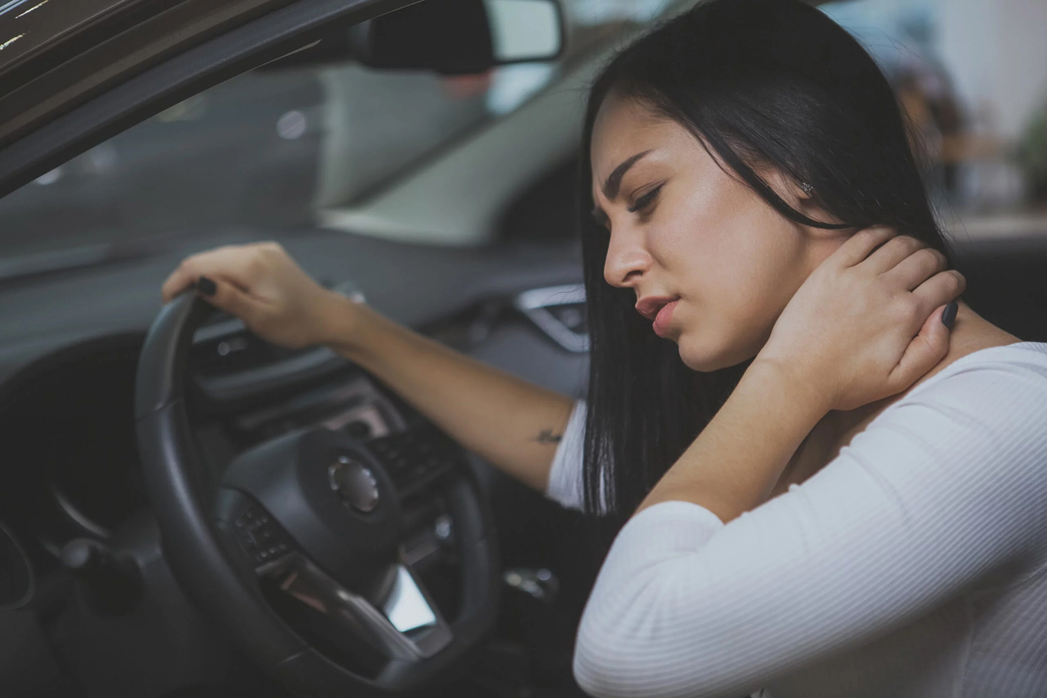 Woman sitting in car holding neck with a pained expression, suggesting neck pain or whiplash.