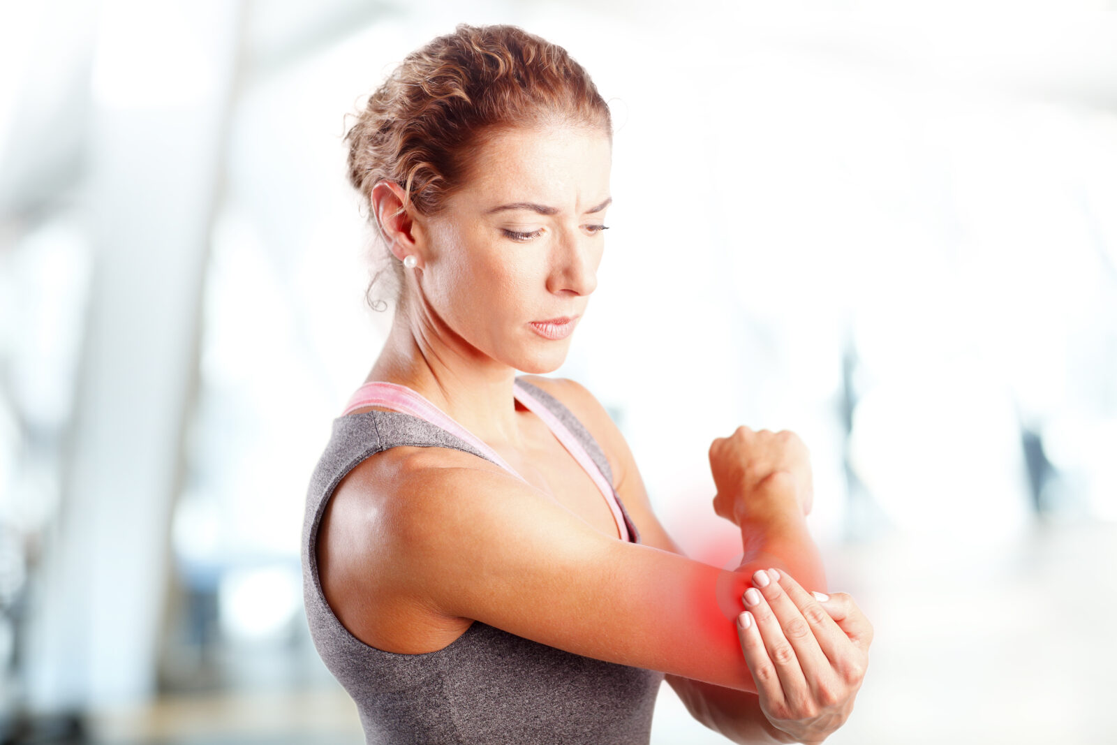 Woman in athletic wear holding her elbow with a red area indicating elbow pain.