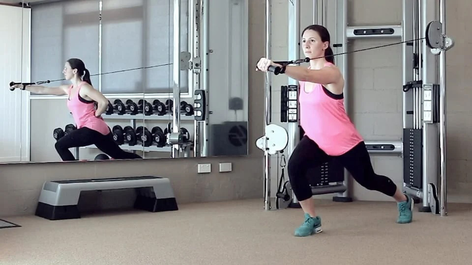 Woman in pink top and black leggings doing a cable machine workout in a gym.