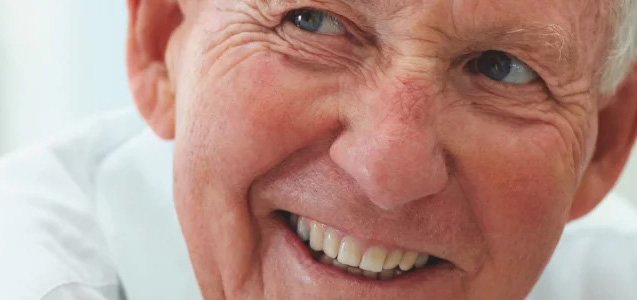 Close-up of a smiling elderly man with blue eyes and white hair.
