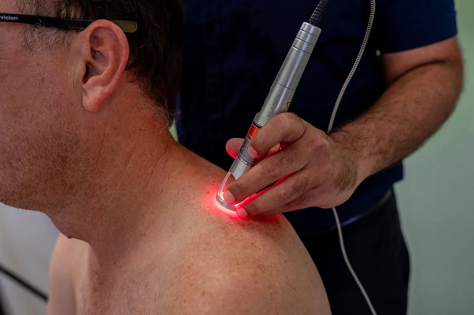 Therapist using a handheld laser device on a man's shoulder for treatment.