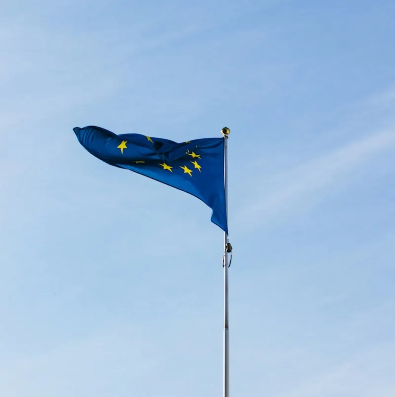 Die Flagge der Europäischen Union mit zwölf gelben Sternen auf blauem Hintergrund weht an einer Fahnenstange vor klarem Himmel.