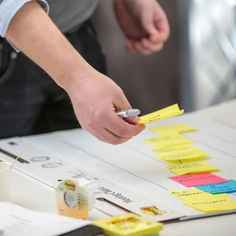 Hand ordnet gelbe Post-it-Notizen auf einem Whiteboard mit Klebeband und Stift in Nahaufnahme.