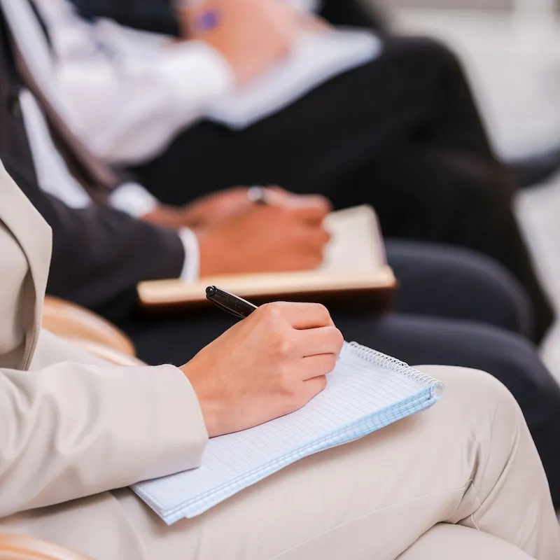 Personen in einer Schulung, die auf Notizblöcken mit Stiften schreiben.