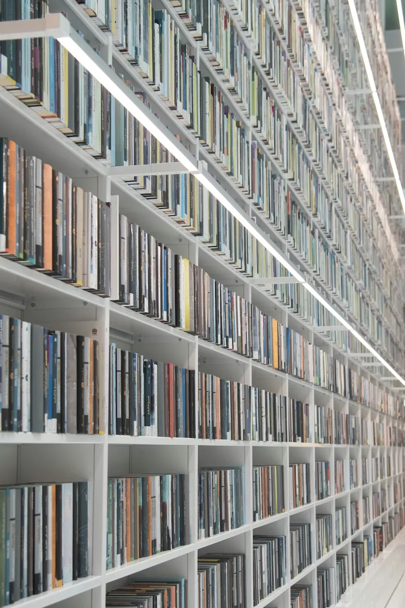 Weißes Bücherregal mit vielen bunten Büchern, die sich bis zur Decke eines hellen Raums erstrecken.