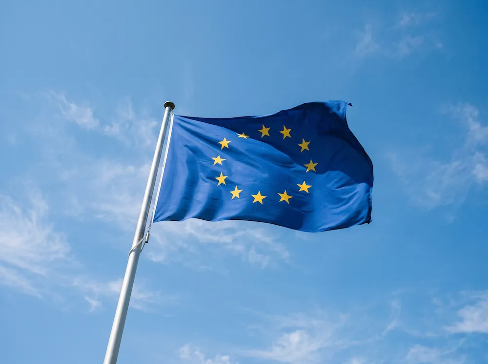 Flagge der Europäischen Union mit zwölf goldenen Sternen im Kreis vor blauem Himmel.