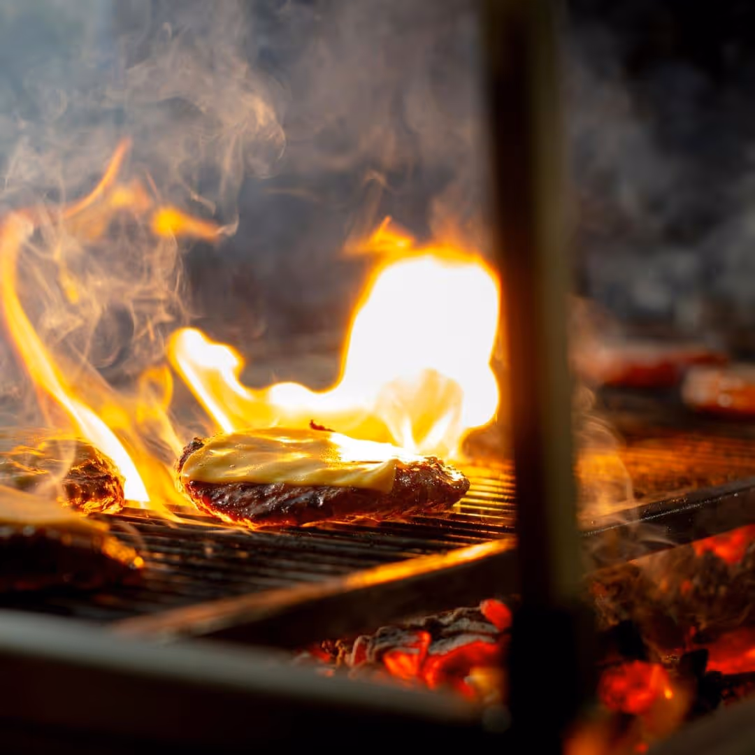 Burger met gesmolten kaas op een hete grill met open vuur tijdens een BBQ catering van De Keukenploeg