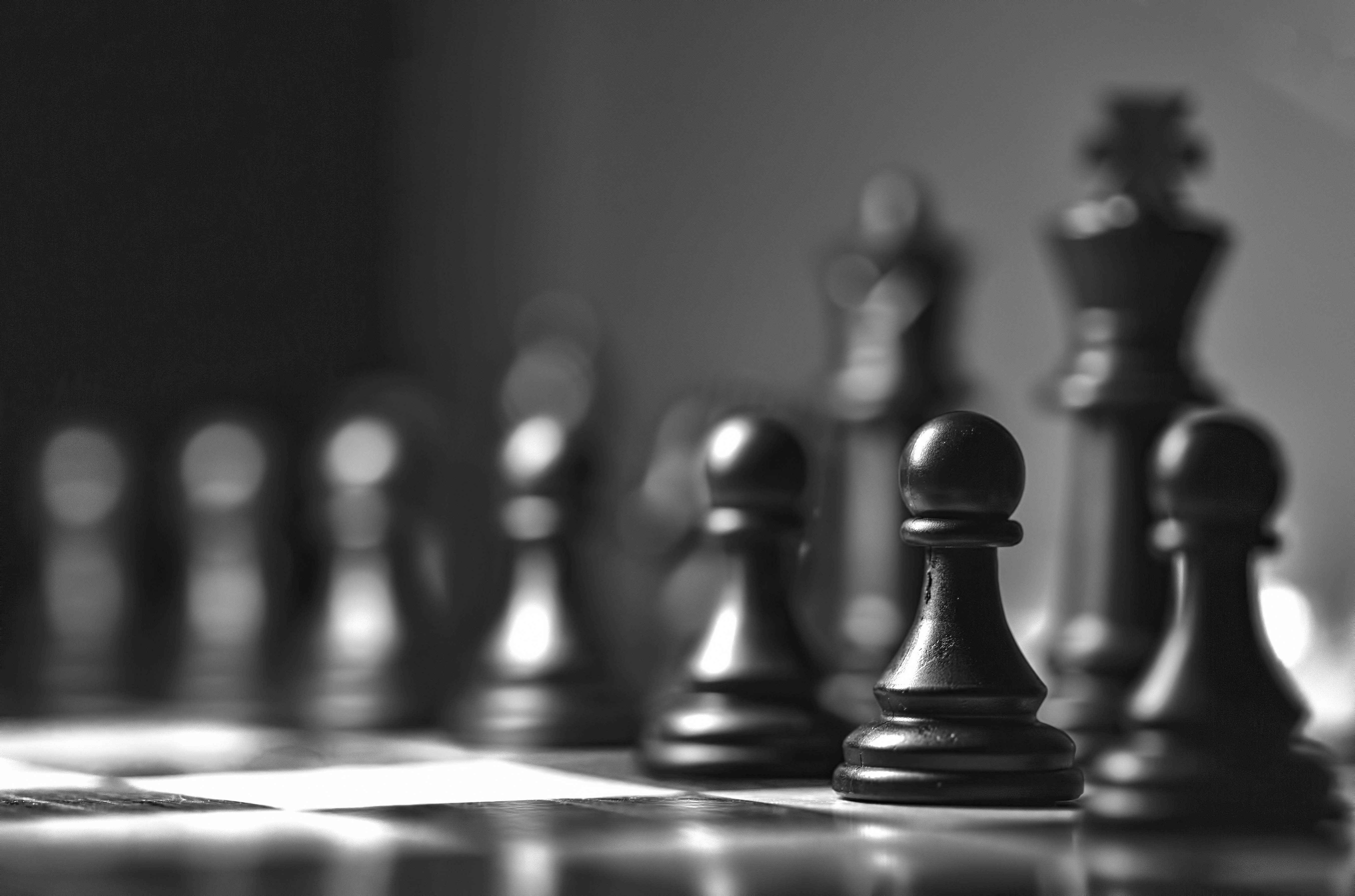 Pièces d'échecs noires en ligne sur un échiquier en noir et blanc avec un focus sur un pion noir devant.