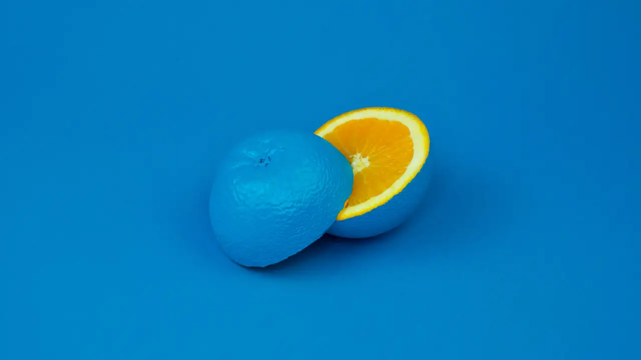 Une orange peinte en bleu est coupée en deux, montrant l'intérieur orange vif.