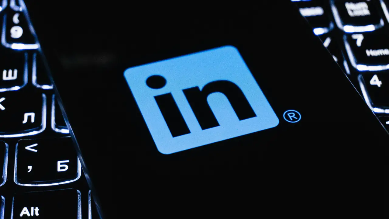 Logo LinkedIn bleu clair sur l'écran d'un smartphone avec clavier en arrière-plan.