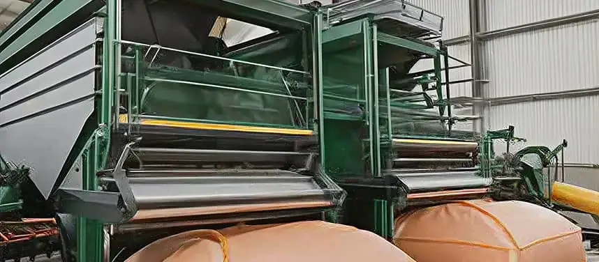 Green industrial machinery inside a warehouse equipped with large orange collection bags.