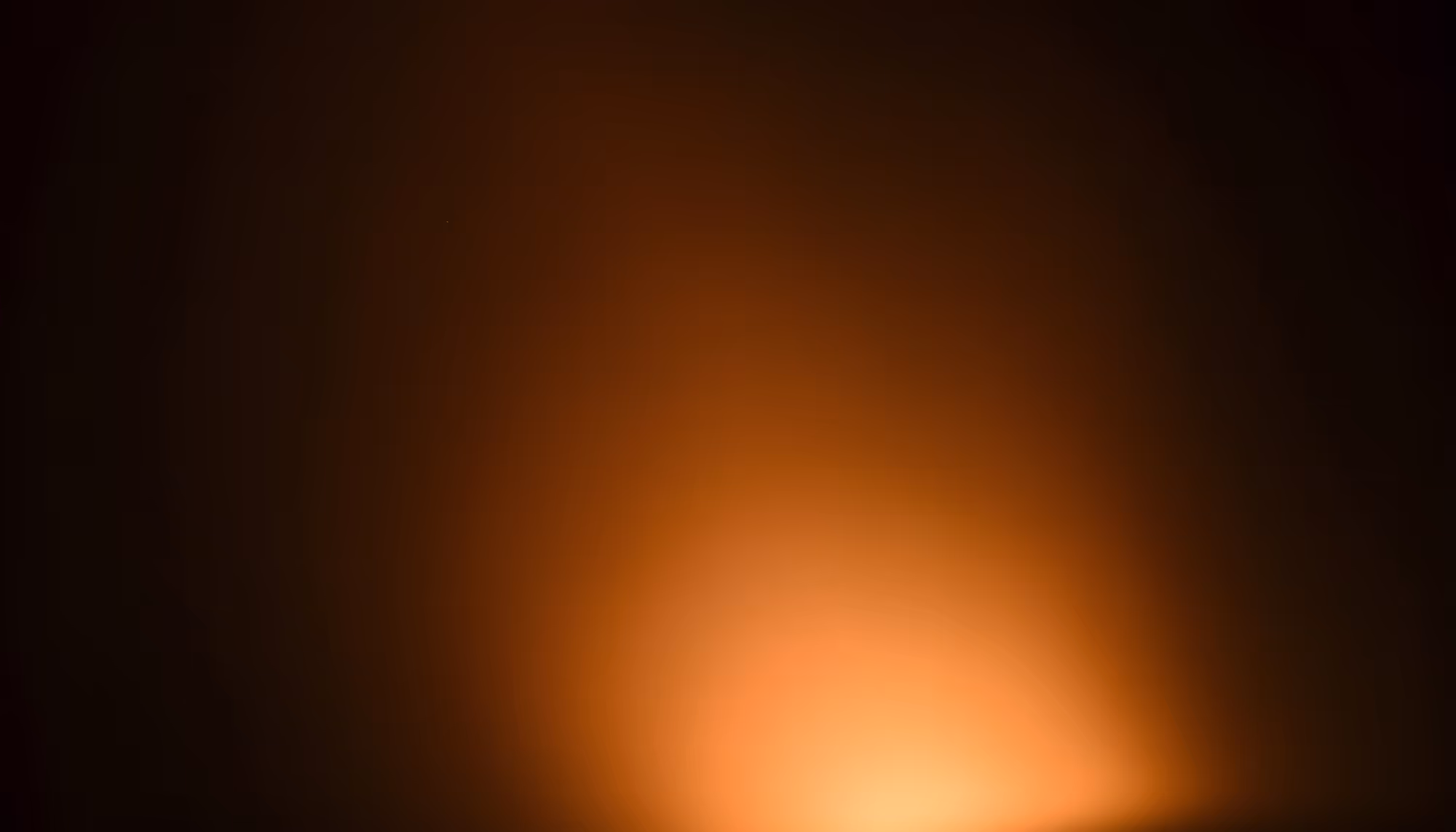 A warm orange glow emanating from a bright light source at the bottom center of an otherwise dark frame, creating a soft radiant bloom against a black background.