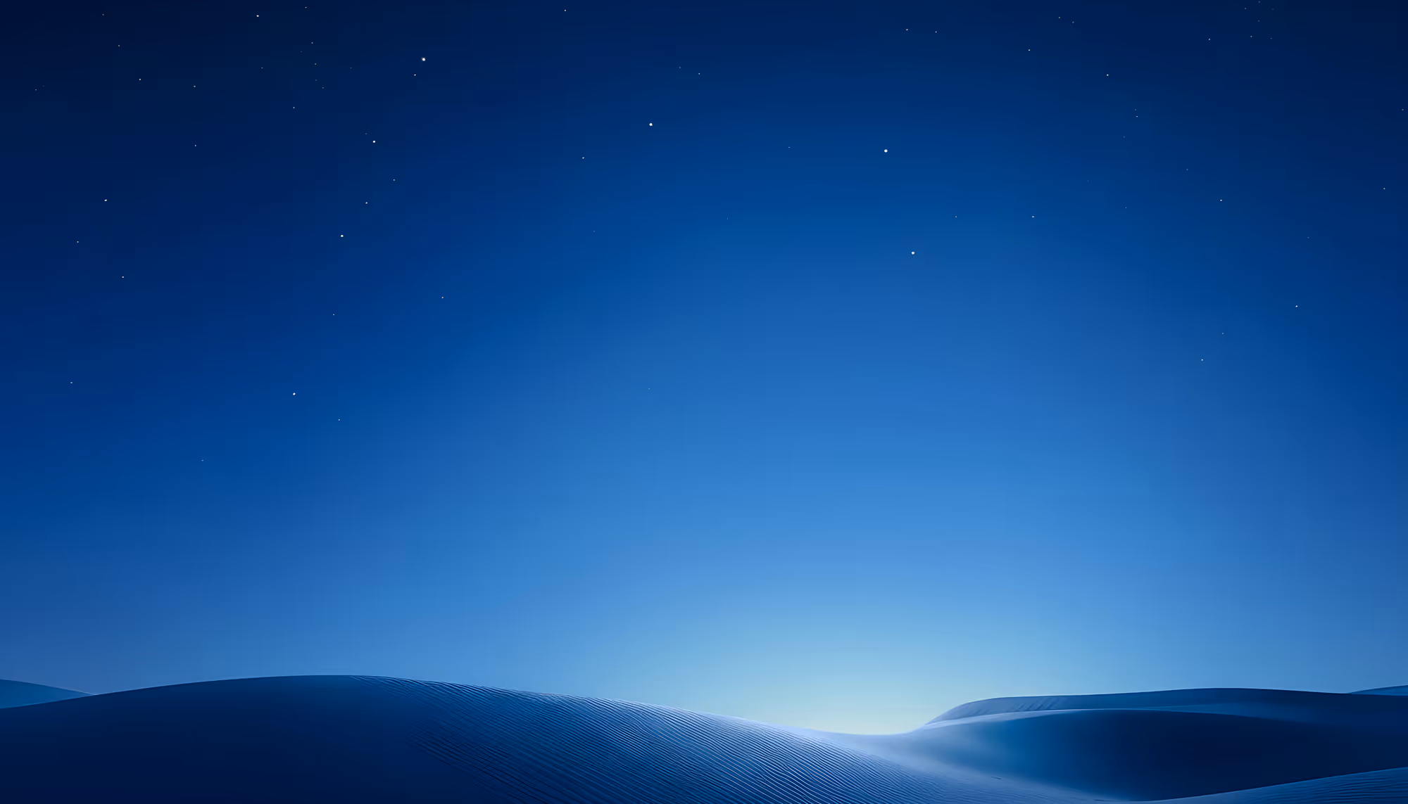 Sand dunes under a deep blue twilight sky with scattered stars, bathed in soft moonlight that creates gentle highlights and shadows across the rippled sand surface.