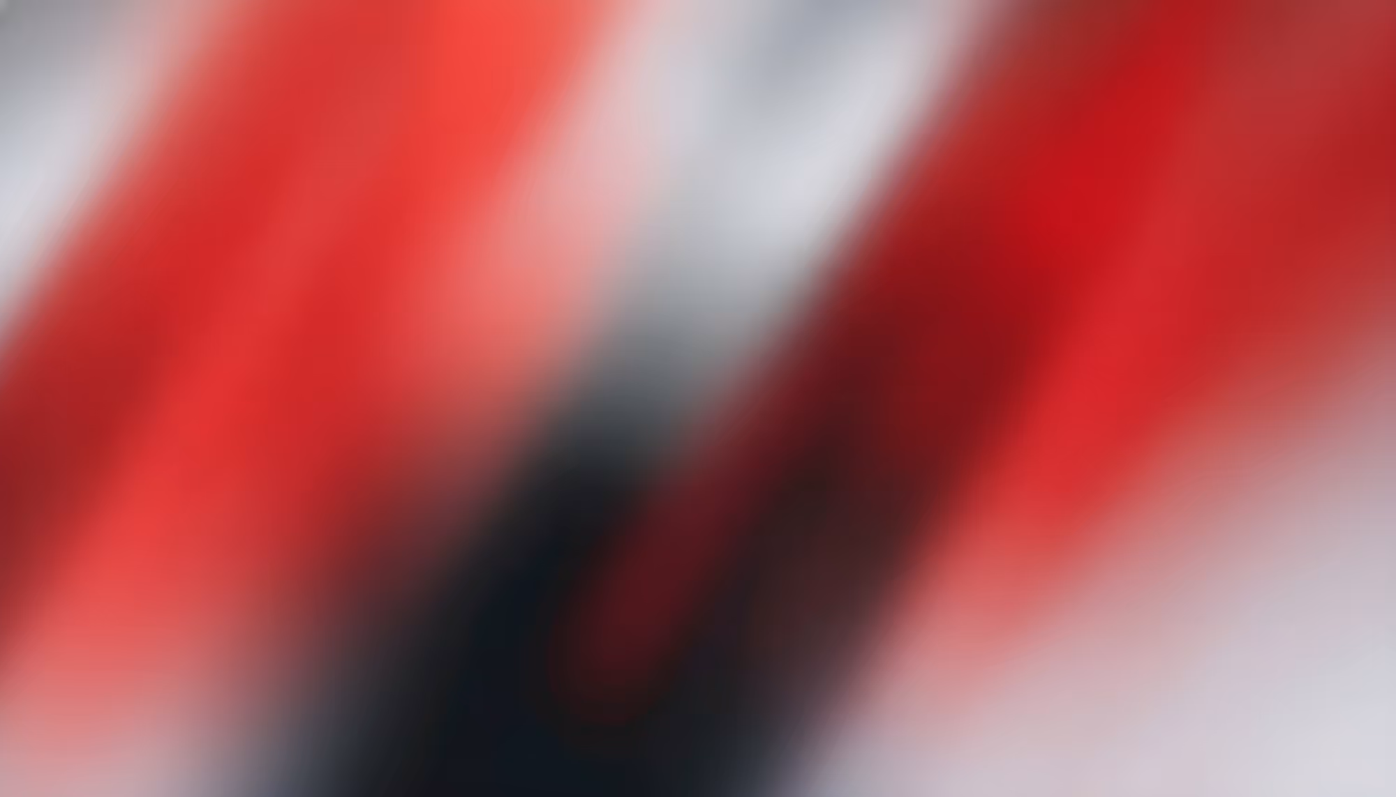 Abstract image with blurred streaks of red and black diagonally across a soft gray background. The colors blend to create a dynamic, vibrant feel.