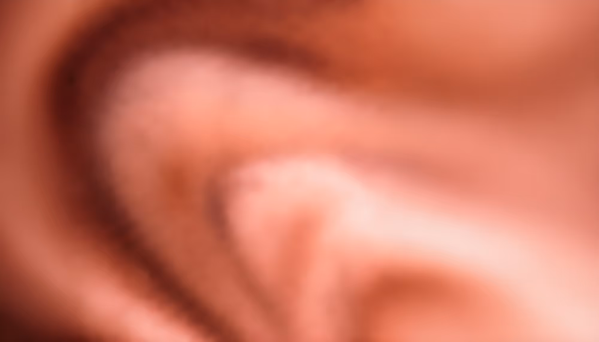 Blurry close-up of an ear with soft pink and peach tones, creating an abstract and indistinct visual, conveying a sense of ambiguity and softness.