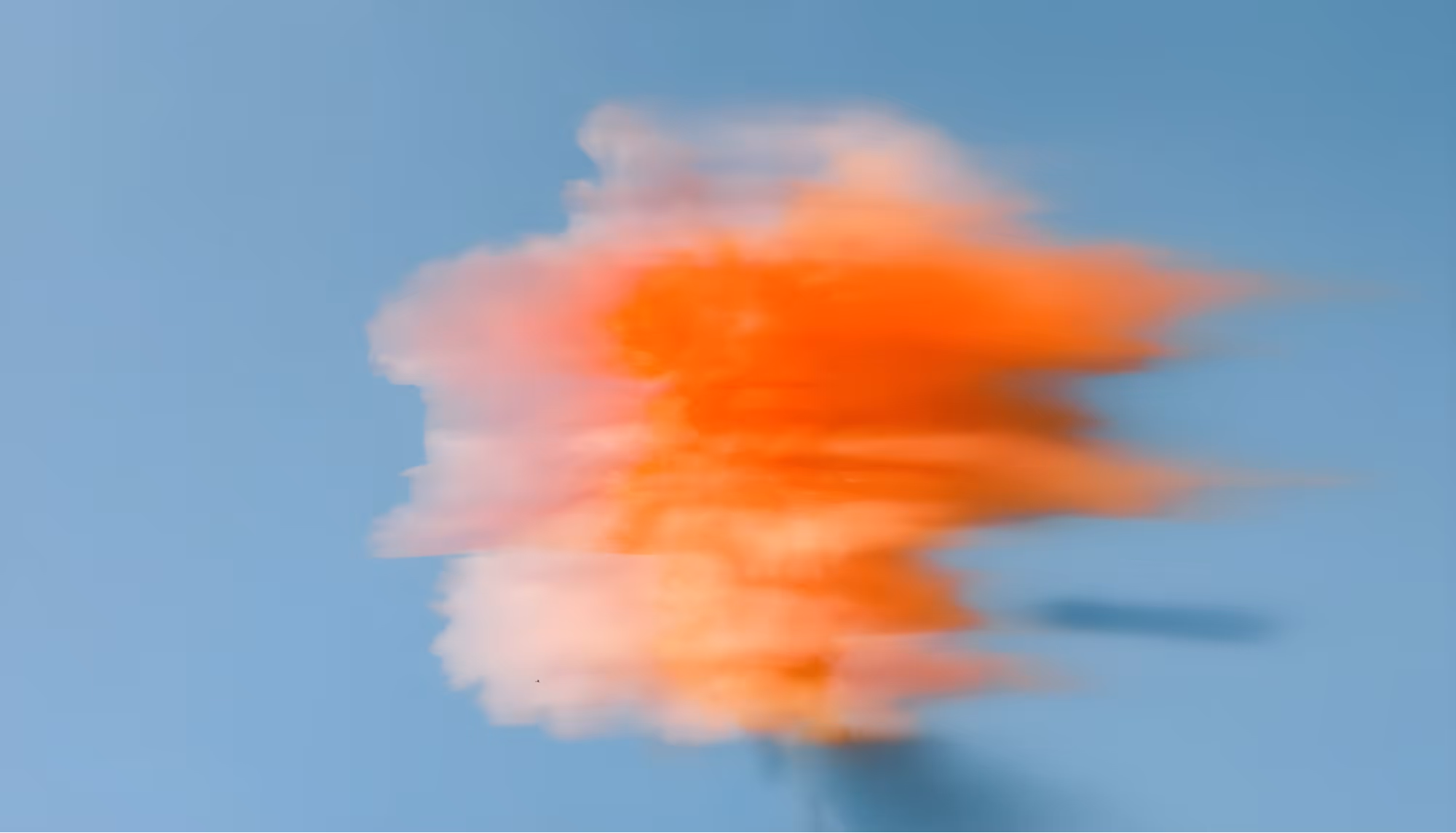 Abstract image of blurred orange and pink hues resembling a cloud against a soft blue background, conveying a sense of motion and calm.