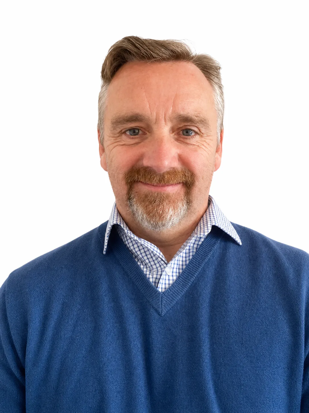 Smiling middle-aged man with grey hair, beard, blue sweater, and checkered shirt on white background.