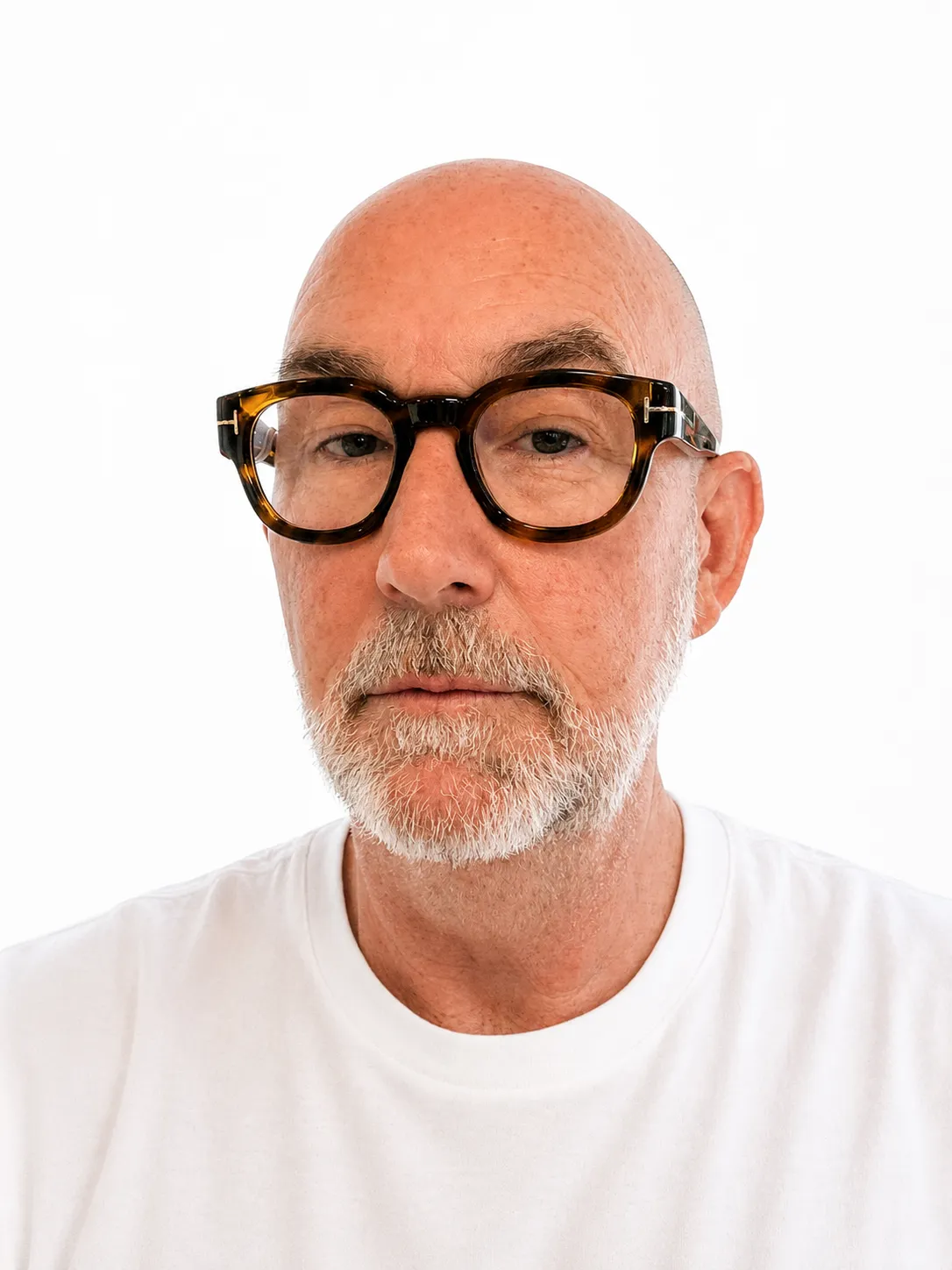 Bald older man with gray beard wearing large tortoiseshell glasses and a white shirt.