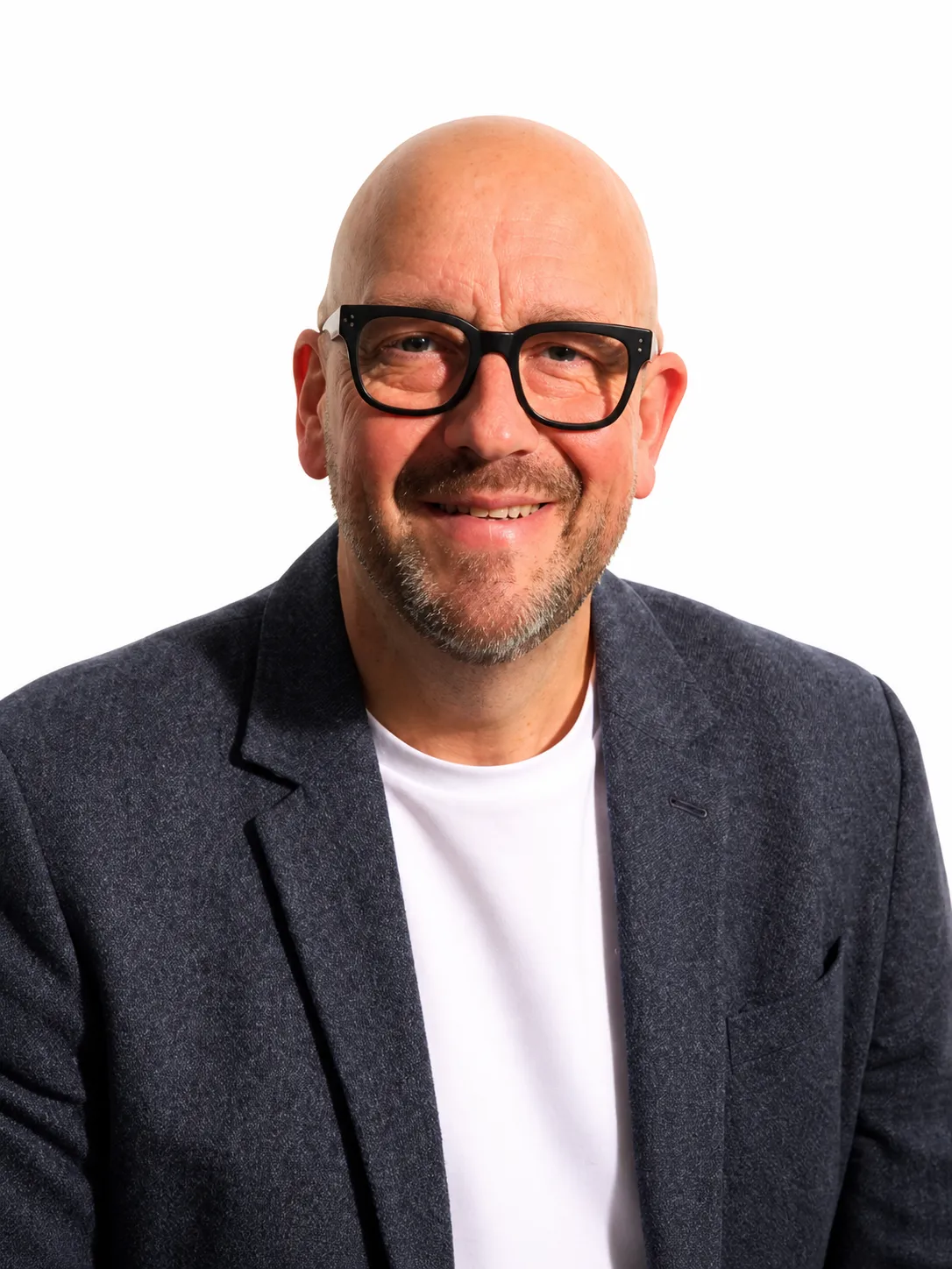 Smiling bald man with glasses wearing a white shirt and dark blazer on a white background.