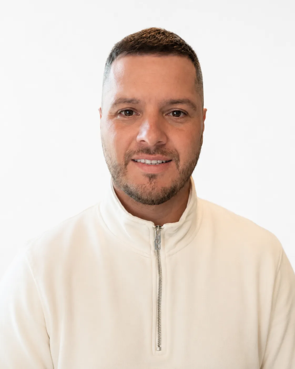 Smiling man with short hair and light beard wearing a white quarter-zip pullover against white background.