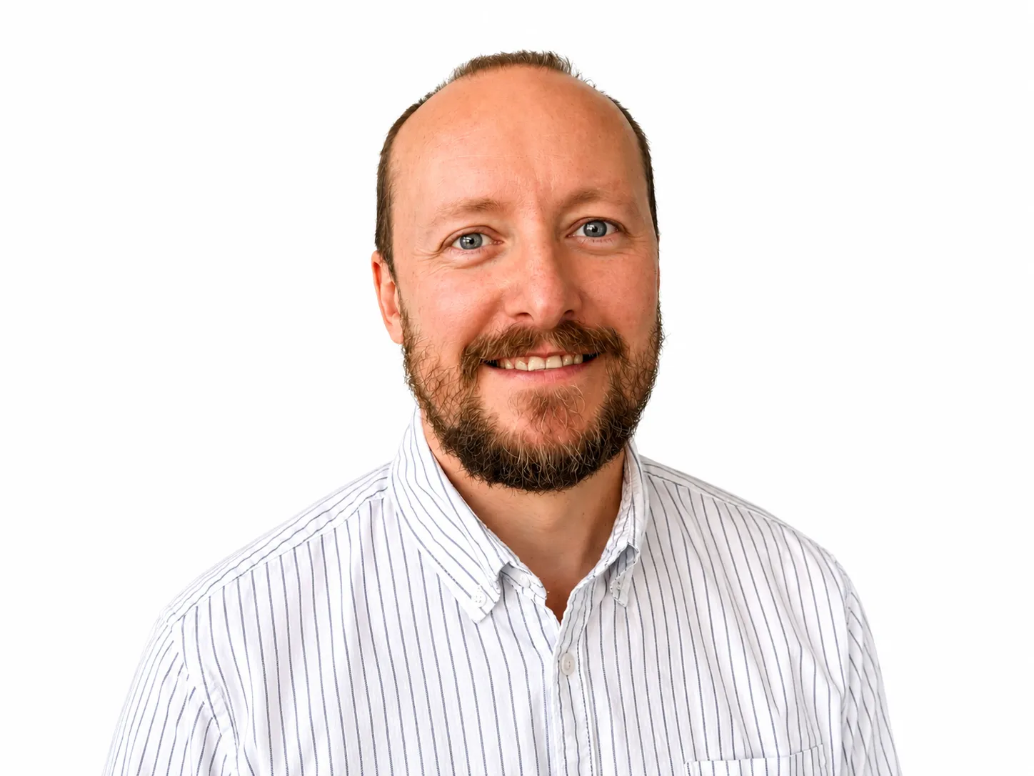 Smiling bald man with a beard wearing a white shirt with thin blue stripes on a white background.
