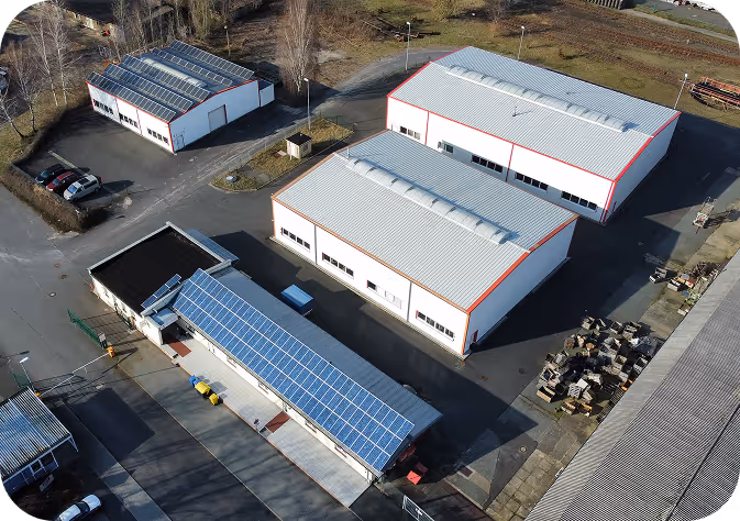 Luftaufnahme eines Industriegebiets mit mehreren Lagerhallen, von denen eine mit Solarpaneelen auf dem Dach ausgestattet ist.