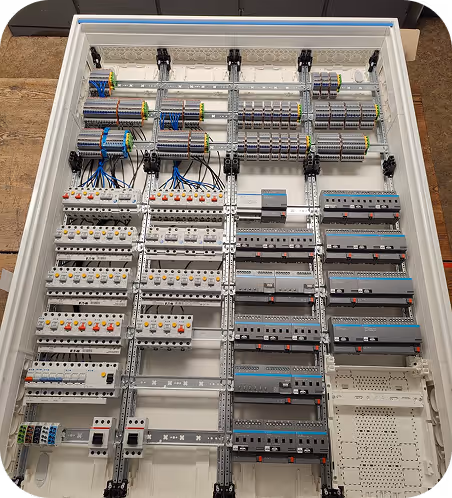 Geöffneter elektrischer Schaltschrank mit Reihen von Sicherungen, Schaltern und verdrahteten Klemmenleisten in organisiertem Layout.