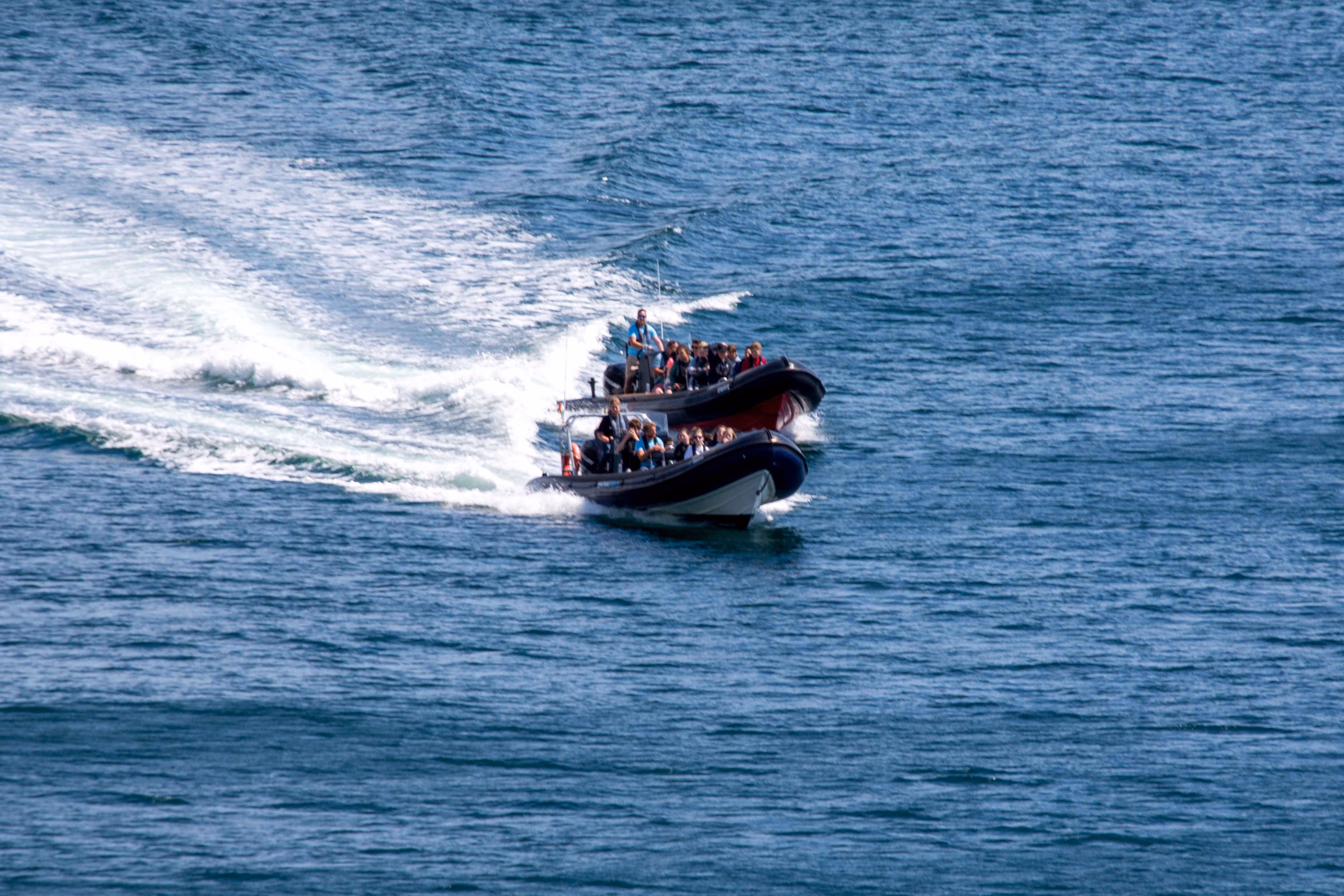 Two motorboats speeding on blue water with passengers seated and creating white water trails.