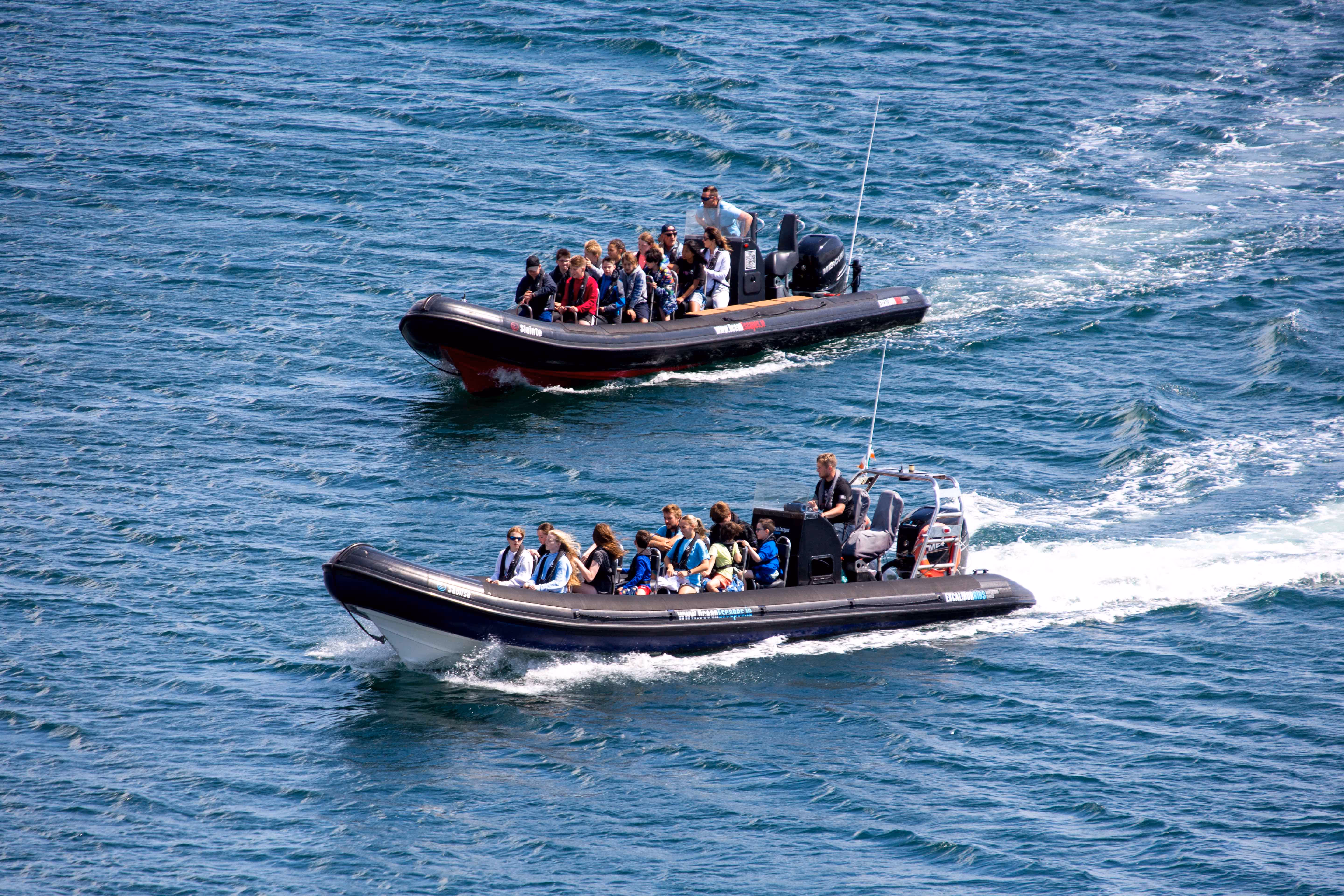 Two black inflatable boats each carrying groups of people cruising on blue ocean water.