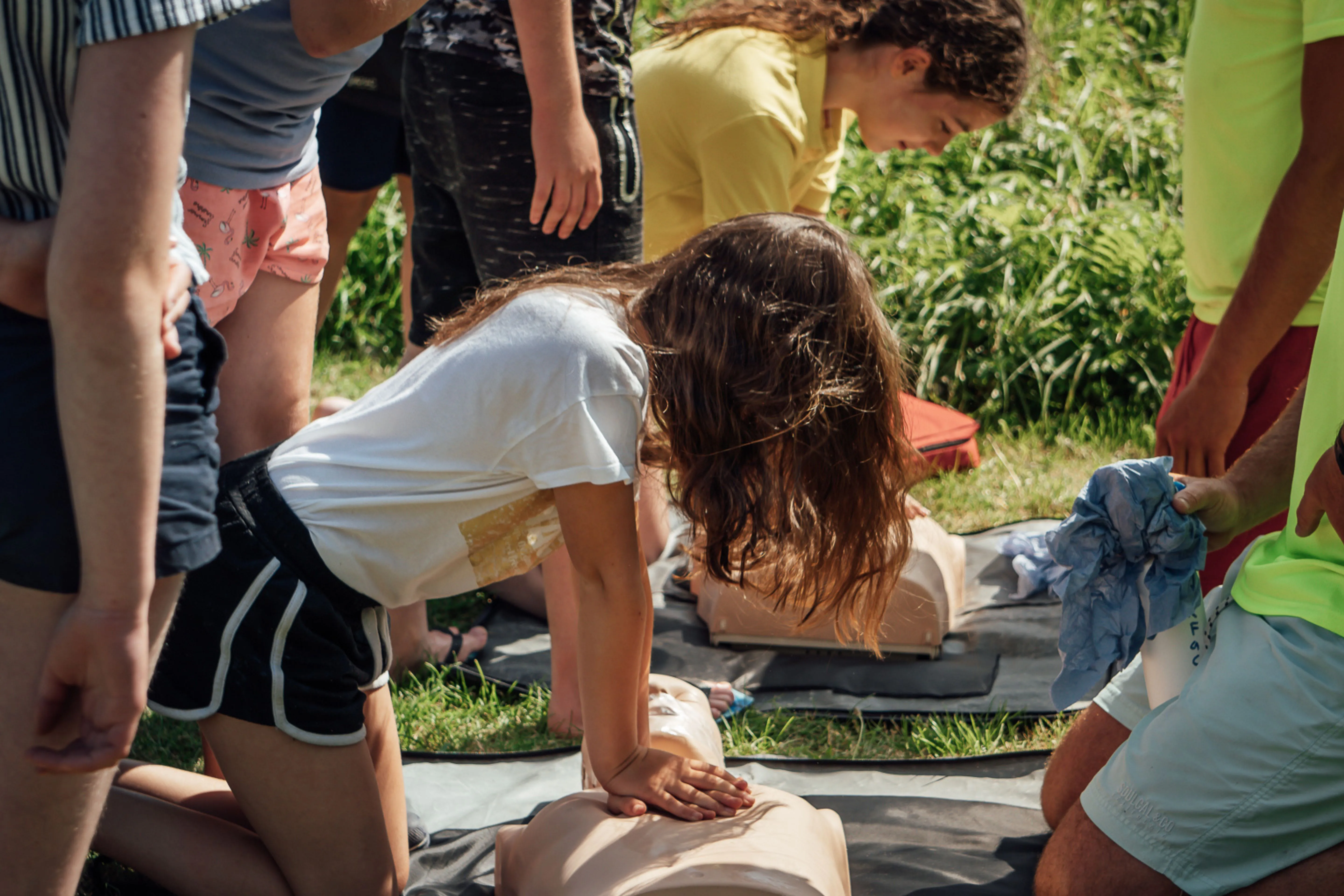 A group of people outdoors practicing chest compressions on CPR training mannequins on mats.