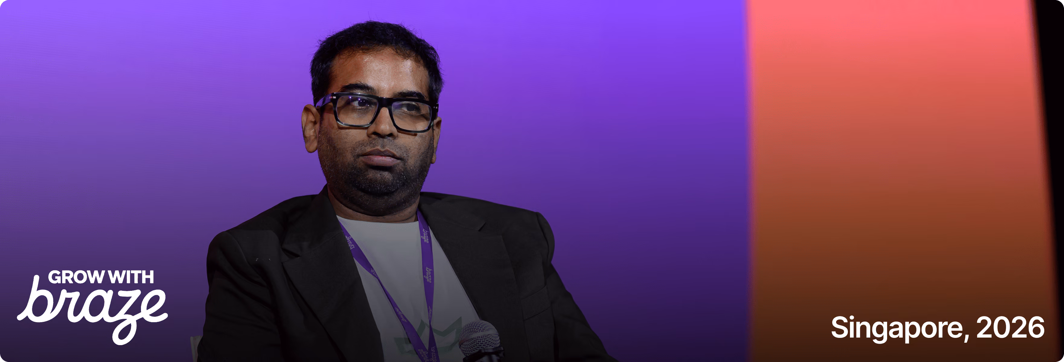 Man with glasses in black blazer and lanyard, purple and orange gradient background, text 'Singapore, 2026'.