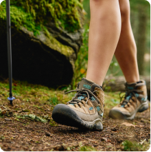 Close-up of a hiker's boots walking on a dirt trail in a green forest.